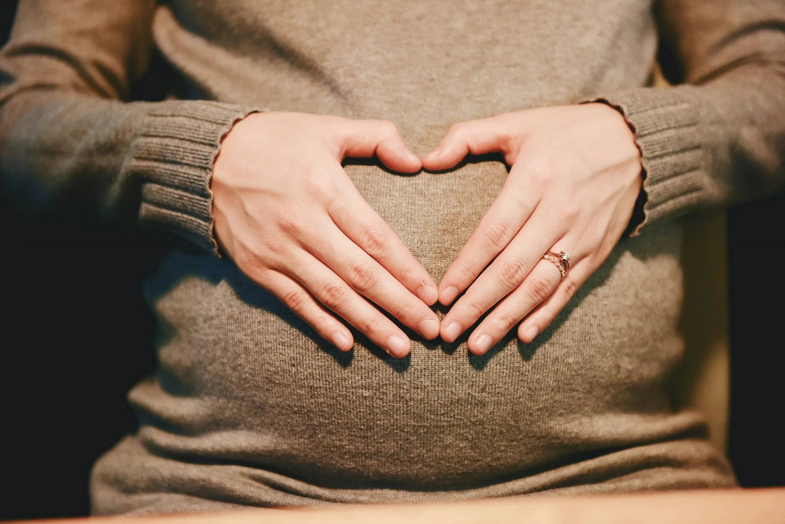 a women holding her belly with her hands shaping a heart.